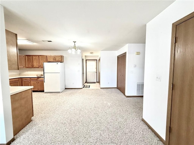 kitchen with brown cabinetry, freestanding refrigerator, light countertops, and visible vents