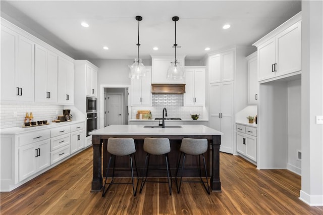 kitchen with dark wood-style flooring, a kitchen island with sink, and white cabinets