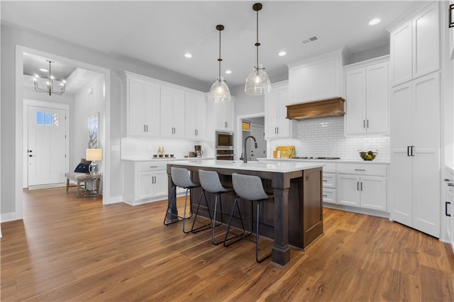 kitchen with wood finished floors, premium range hood, white cabinetry, light countertops, and a kitchen bar