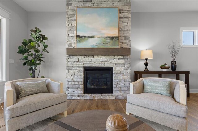 living area with baseboards, a stone fireplace, and wood finished floors