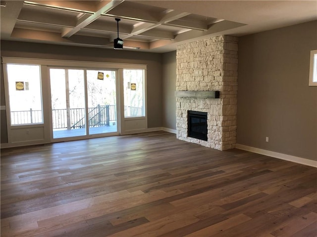 unfurnished living room with baseboards, a stone fireplace, beamed ceiling, and dark wood-type flooring