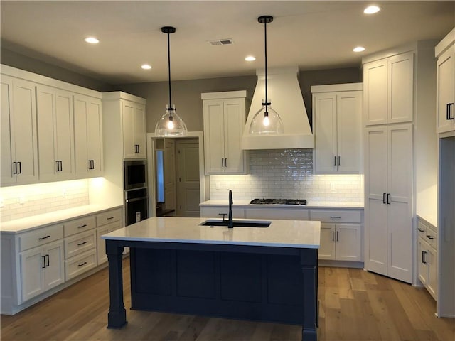 kitchen with light wood finished floors, a sink, visible vents, decorative backsplash, and custom range hood