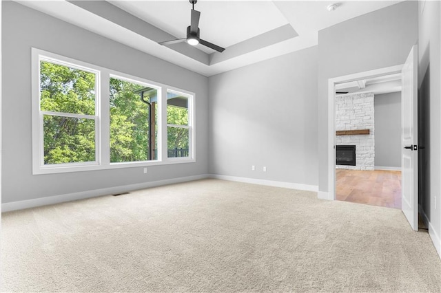 17147 S Heatherwood St, Olathe, KS 66062 - empty room with carpet, ceiling fan, baseboards, a stone fireplace, and a raised ceiling