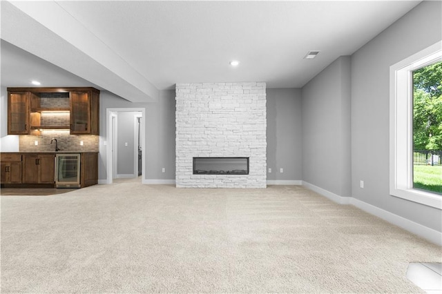 17147 S Heatherwood St, Olathe, KS 66062 - unfurnished living room featuring wine cooler, a sink, light colored carpet, a stone fireplace, and recessed lighting