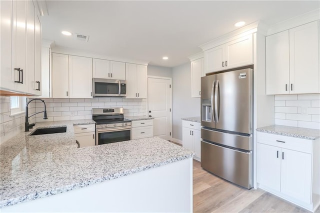 kitchen featuring visible vents, light wood-style flooring, appliances with stainless steel finishes, a sink, and light stone countertops