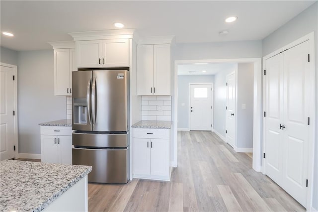 kitchen with stainless steel refrigerator with ice dispenser, backsplash, light wood-style floors, white cabinets, and light stone countertops