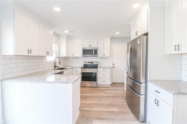 kitchen with stainless steel appliances, tasteful backsplash, white cabinets, a sink, and light wood-type flooring