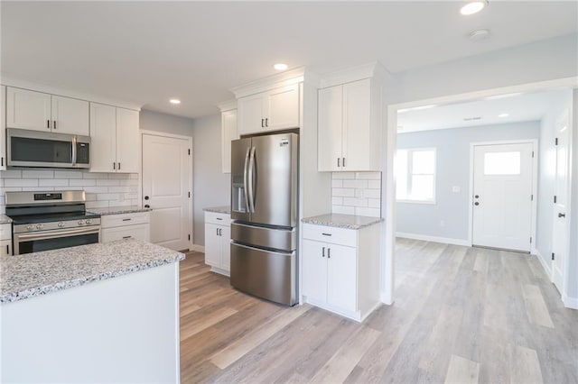 kitchen featuring light wood-type flooring, appliances with stainless steel finishes, white cabinets, and decorative backsplash