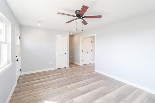 spare room with light wood finished floors, a ceiling fan, visible vents, and baseboards