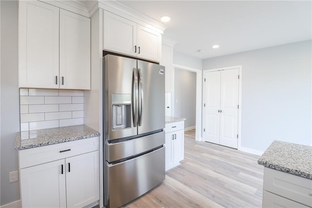 kitchen with light wood-type flooring, stainless steel fridge, light stone counters, and backsplash