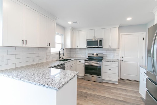 kitchen featuring light stone counters, stainless steel appliances, light wood-style floors, white cabinetry, and a sink