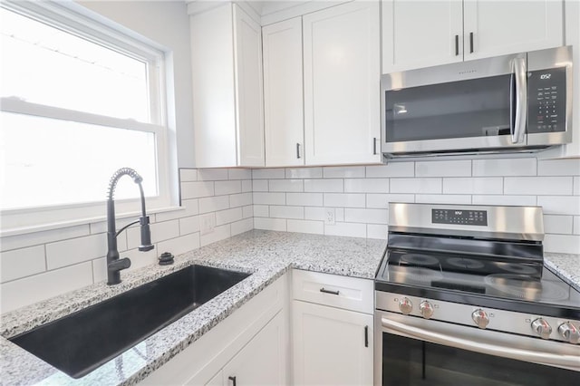 kitchen featuring appliances with stainless steel finishes, decorative backsplash, a sink, and white cabinets