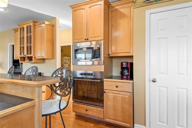 15498 Cedar Ln, Basehor, KS 66007 - kitchen with stainless steel microwave, oven, light wood finished floors, glass insert cabinets, and dark countertops