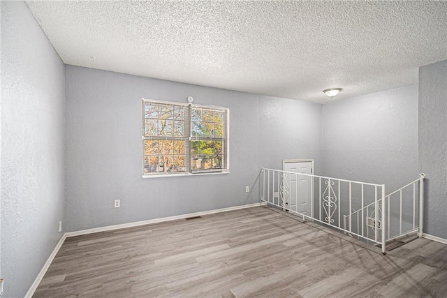 empty room featuring baseboards, wood finished floors, and a textured wall