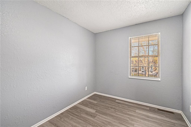 unfurnished room featuring a textured wall, baseboards, and wood finished floors