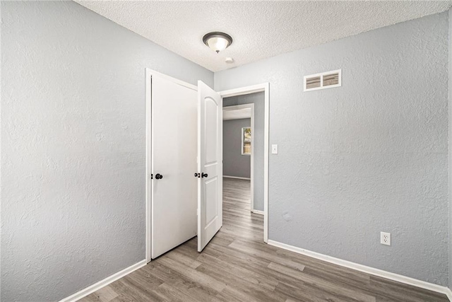 interior space featuring visible vents, wood finished floors, baseboards, and a textured wall