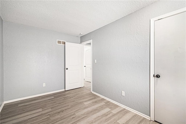 unfurnished bedroom featuring visible vents, baseboards, wood finished floors, a textured wall, and a textured ceiling