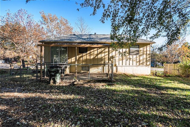 back of property featuring a lawn, board and batten siding, roof with shingles, and fence