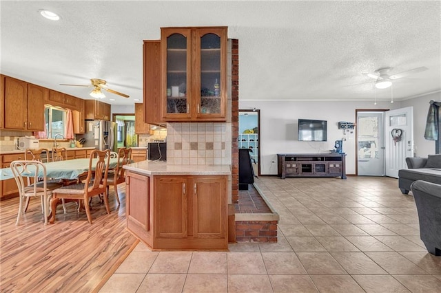 kitchen with tasteful backsplash, light countertops, a ceiling fan, open floor plan, and stainless steel fridge