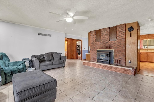 living area featuring visible vents, ceiling fan, a wood stove, a textured ceiling, and light tile patterned flooring