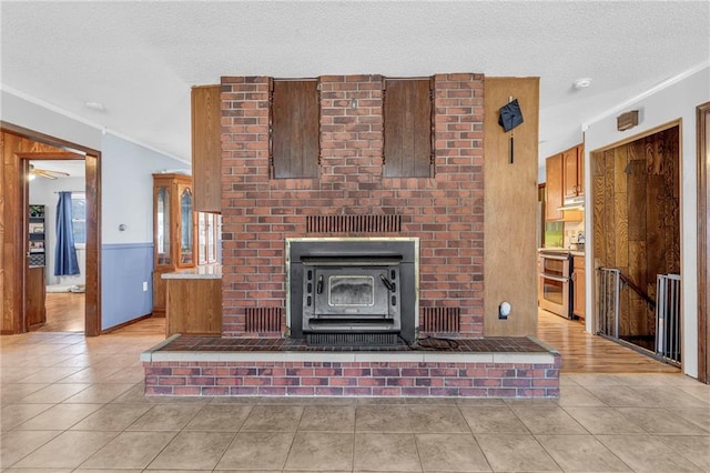 unfurnished living room with a textured ceiling, a wainscoted wall, a wood stove, and tile patterned floors