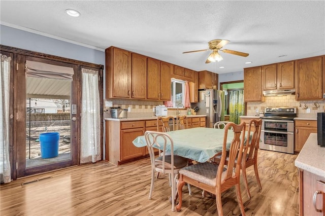 kitchen with light wood finished floors, stainless steel appliances, light countertops, visible vents, and under cabinet range hood