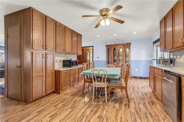 kitchen featuring brown cabinets, light countertops, appliances with stainless steel finishes, light wood-style floors, and wainscoting