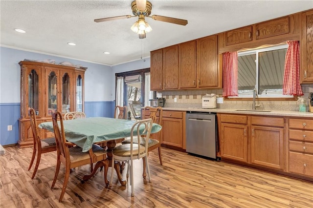 kitchen featuring wainscoting, a sink, light wood-style flooring, and stainless steel dishwasher