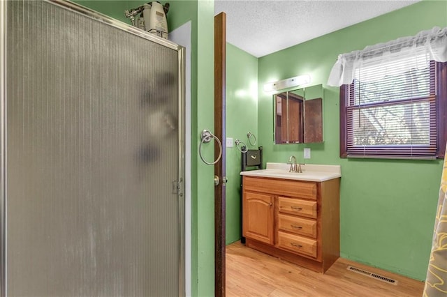 full bathroom with a stall shower, visible vents, wood finished floors, a textured ceiling, and vanity