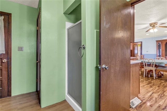 interior space featuring a textured ceiling, ceiling fan, wood finished floors, vanity, and a shower with door