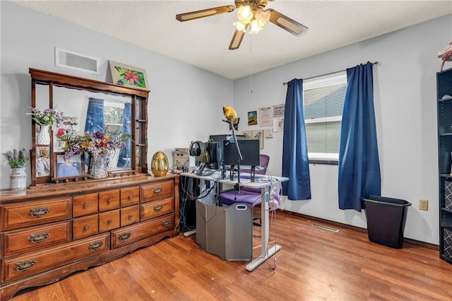 office area featuring light wood-style floors, a ceiling fan, visible vents, and a textured ceiling