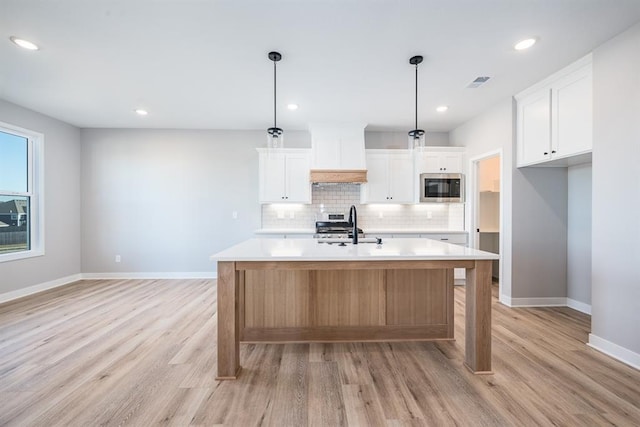 kitchen with stainless steel appliances, visible vents, light wood-style floors, light countertops, and backsplash