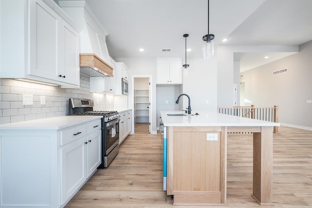 kitchen with a center island with sink, decorative backsplash, appliances with stainless steel finishes, a sink, and light wood-type flooring