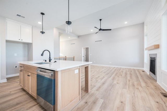 kitchen featuring visible vents, stainless steel dishwasher, light wood-style floors, a large fireplace, and a sink