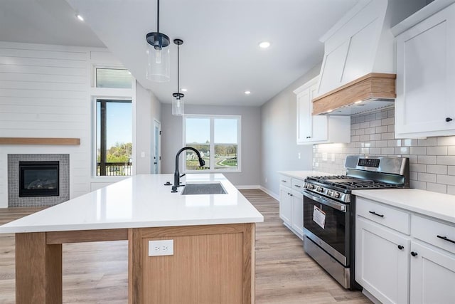 kitchen with decorative backsplash, stainless steel range with gas stovetop, custom exhaust hood, light wood-type flooring, and a sink