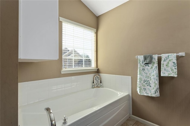 bathroom with tile patterned flooring, vaulted ceiling, a bath, and baseboards