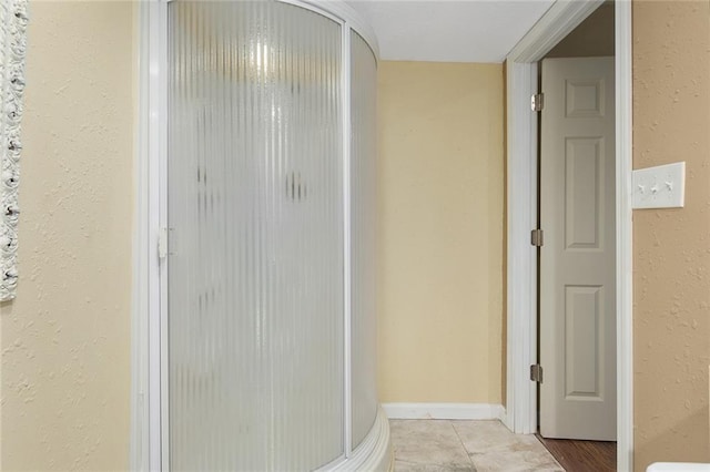 bathroom with tile patterned flooring, a shower stall, and a textured wall