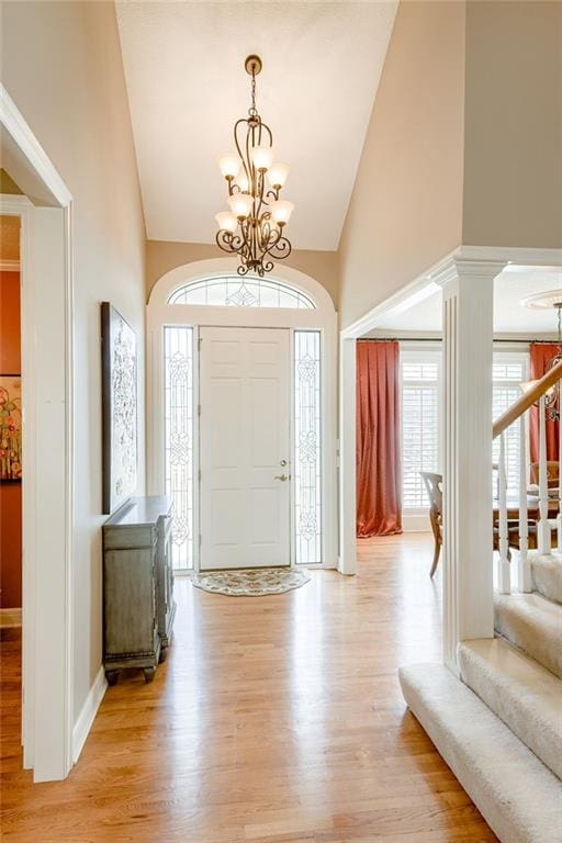 foyer entrance featuring high vaulted ceiling, an inviting chandelier, light wood finished floors, decorative columns, and stairs