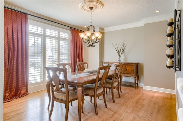 dining area featuring light wood-type flooring, a textured ceiling, an inviting chandelier, crown molding, and baseboards