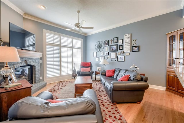 living room with baseboards, light wood finished floors, ceiling fan, a stone fireplace, and ornamental molding