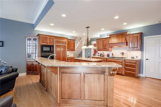 kitchen with light wood-type flooring, a spacious island, custom range hood, built in appliances, and tasteful backsplash