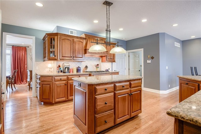 kitchen with light wood finished floors, visible vents, brown cabinets, and light stone countertops