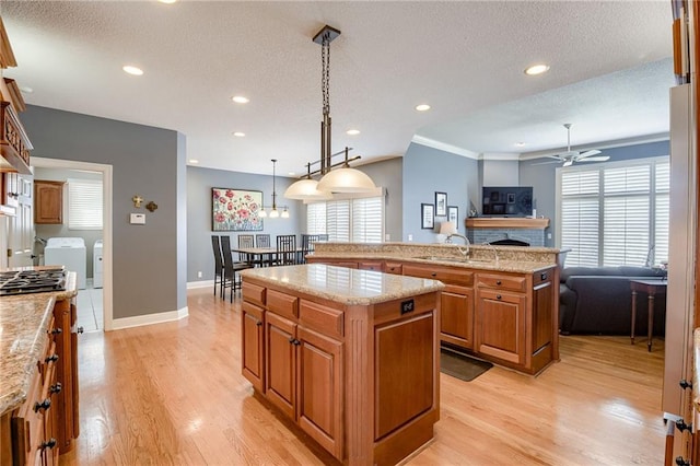 kitchen featuring washing machine and clothes dryer, a center island with sink, brown cabinets, light wood-style floors, and a sink