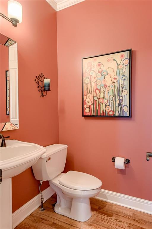 half bathroom with wood finished floors, baseboards, ornamental molding, a sink, and toilet