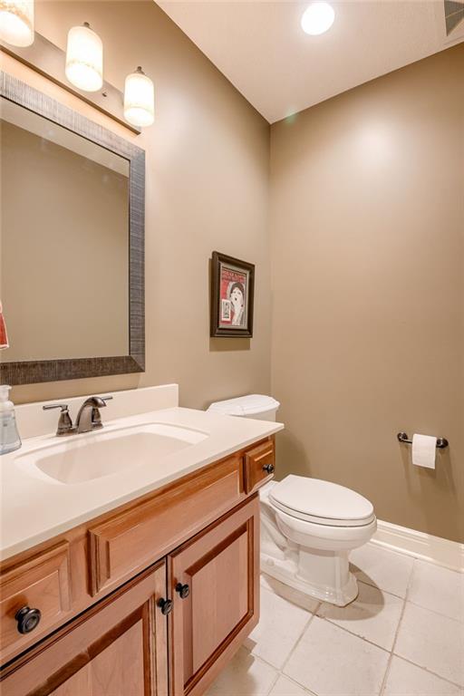 half bath featuring tile patterned floors, toilet, vanity, and baseboards