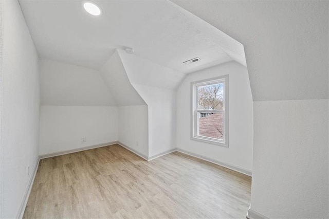 additional living space featuring visible vents, a textured ceiling, wood finished floors, baseboards, and vaulted ceiling