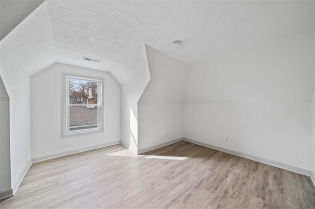 additional living space featuring baseboards, a textured ceiling, wood finished floors, and vaulted ceiling