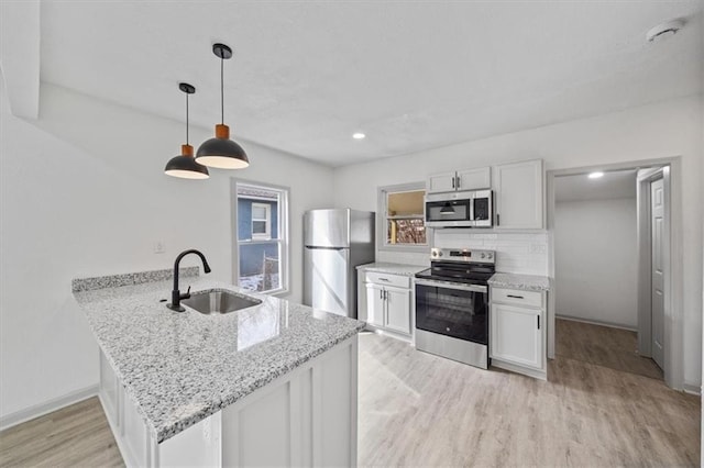 kitchen with a sink, backsplash, light wood-style floors, appliances with stainless steel finishes, and a peninsula