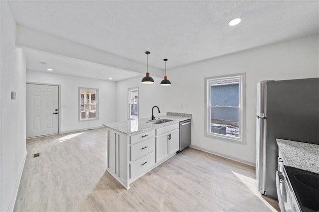 kitchen with light wood-style flooring, a sink, appliances with stainless steel finishes, a peninsula, and light stone countertops