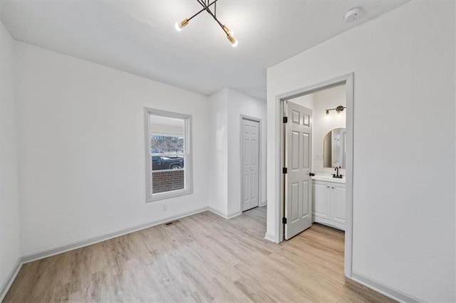 unfurnished bedroom featuring visible vents, baseboards, an inviting chandelier, ensuite bath, and light wood-style flooring